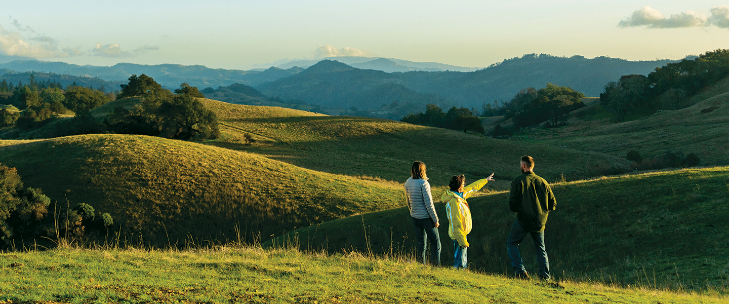 Grand vista of hill tops at sunset with 3 people in the foreground