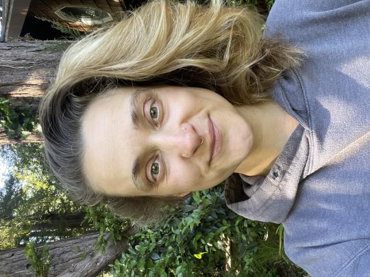 Woman taking a selfie and smiling in front of trees.